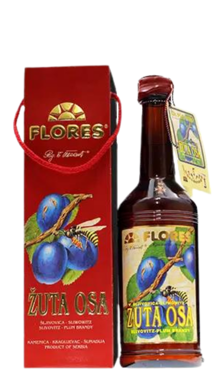 A bottle of Flores Zuta Osa Brandy in a gift box with a red and blue label featuring an image of a plum fruit. The box is presented with a bow and has the brand name 'Flores' visible.